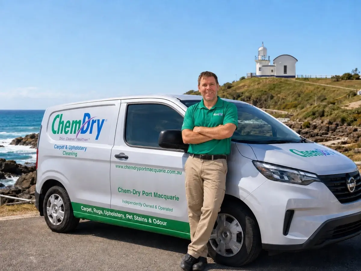 The Chem-Dry Port Macquarie operator in a green Chem-Dry polo, smiling beside the Chem-Dry Port Macquarie van, with Tacking Point Lighthouse and the ocean behind