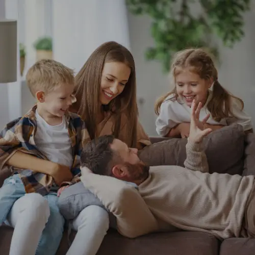 A family of four laughing together on a fabric sofa